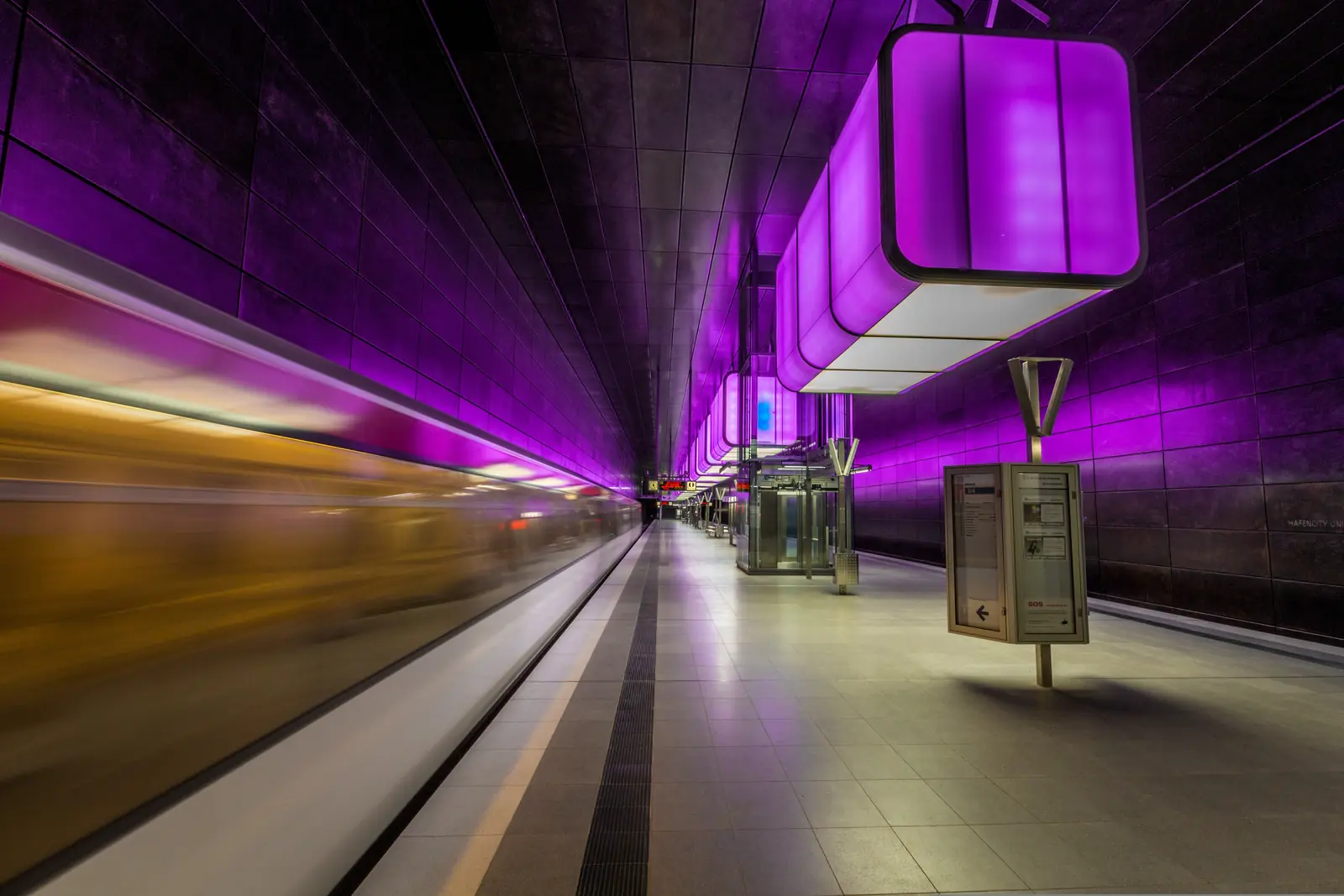 U-Bahn-Station HafenCity Universität in Hamburg mit violetter Beleuchtung und einfahrender Bahn